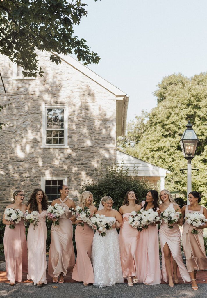 a group of women standing next to each other in front of a brick building holding bouquets