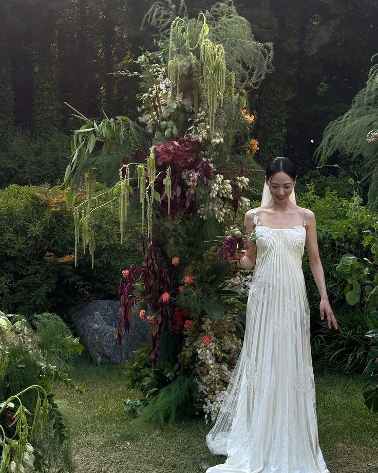 a woman in a wedding dress standing next to a flower covered tree and shrubbery