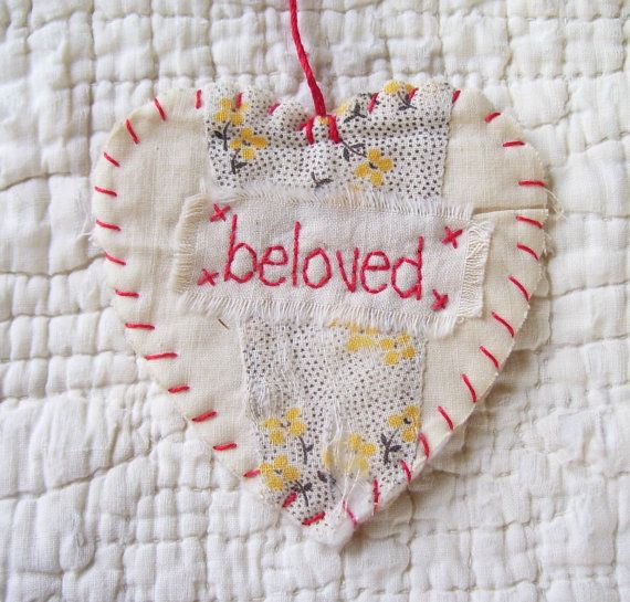 a heart shaped ornament with the word beloved written in red and yellow thread