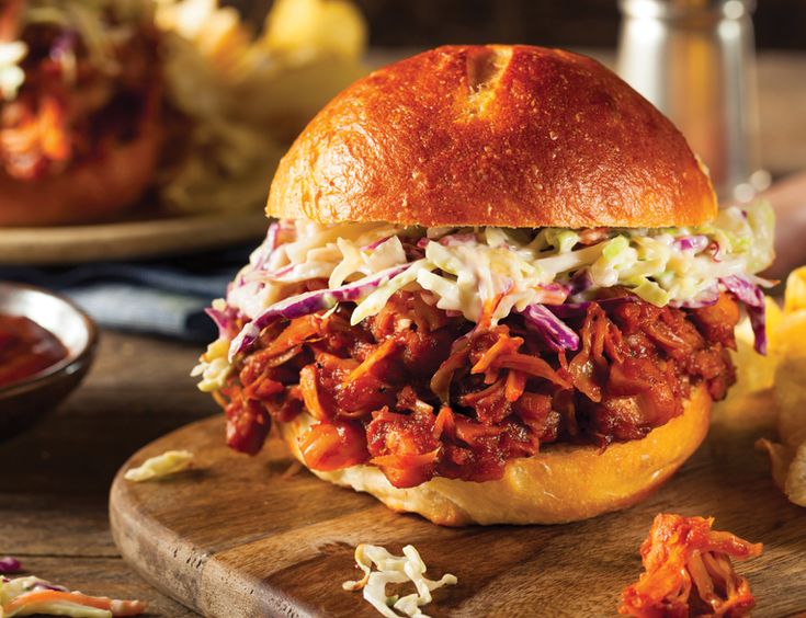 a pulled pork sandwich with cole slaw on a wooden cutting board