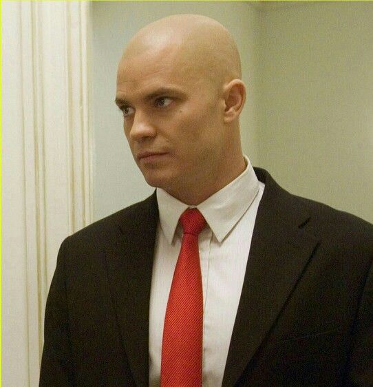 a bald man in a suit and tie holding a pen looking at the camera with an intense look on his face