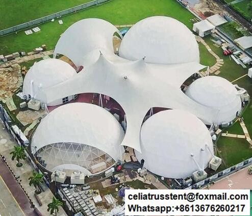 an aerial view of a large white structure in the middle of a green field with trees and buildings around it