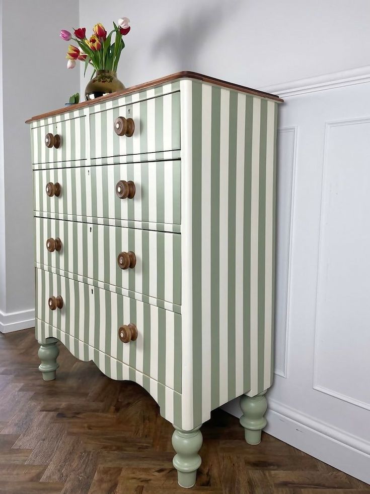 a striped chest of drawers with flowers in a vase sitting on it's top