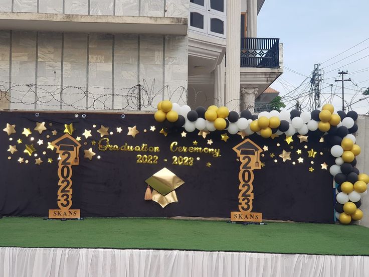 a stage set up with balloons and decorations for a graduation ceremony in front of a building