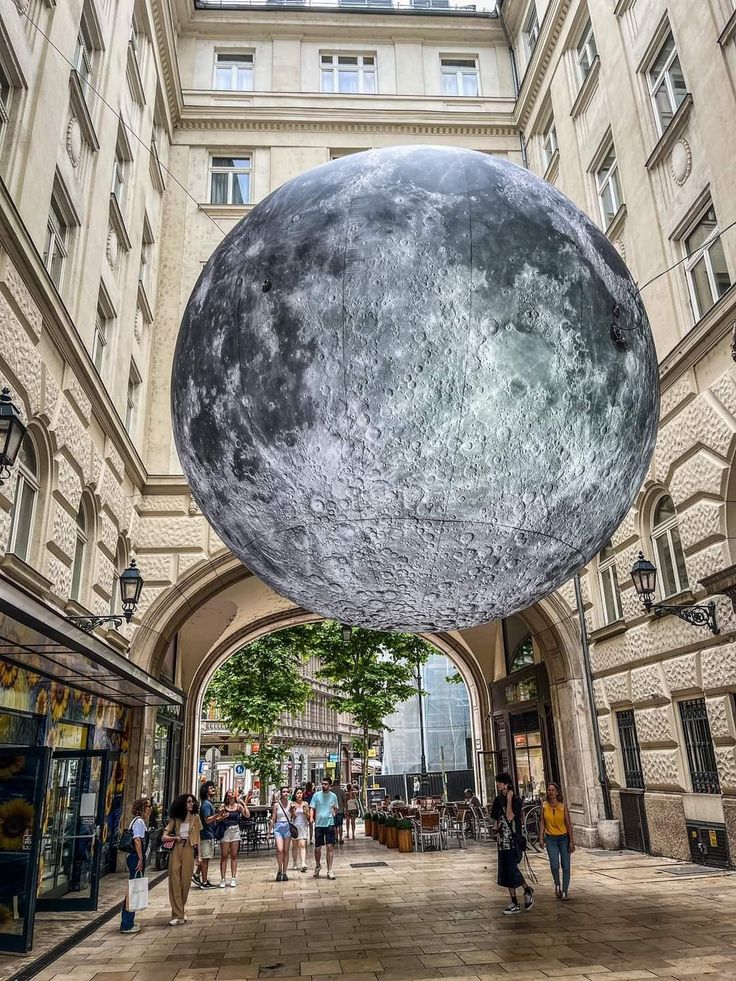 the giant moon sculpture is hanging from the ceiling in an open area with people walking around it