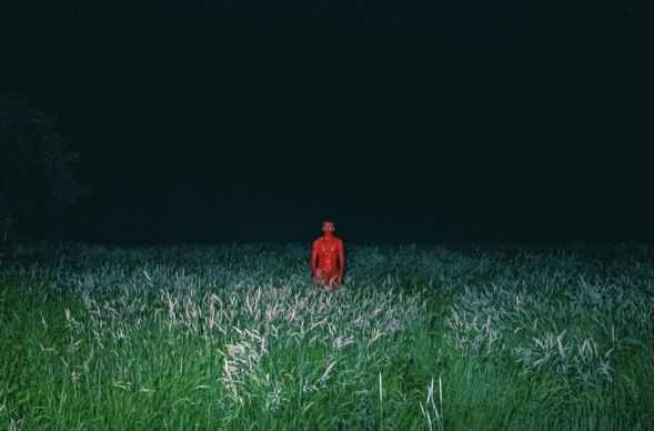 a man standing in the middle of a field at night with his head turned to the side