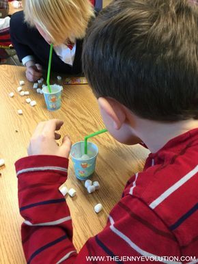 two children sitting at a table with cups and marshmallows on the table