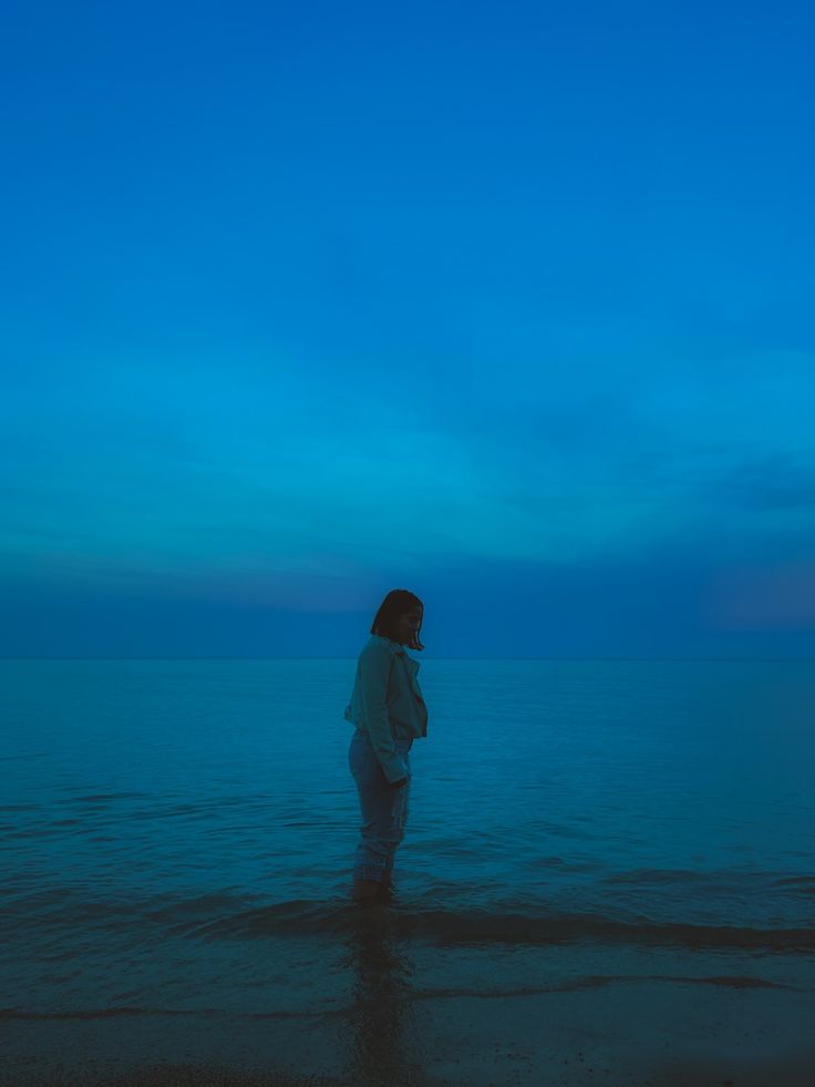 a woman standing in the ocean at night with her back to the camera, looking out into the distance