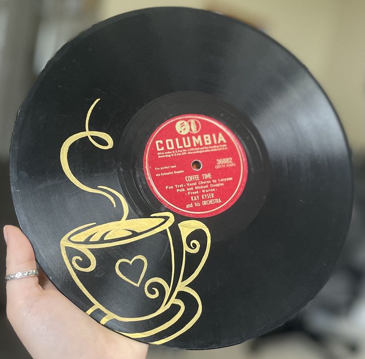 a person holding up a record with a coffee cup on it