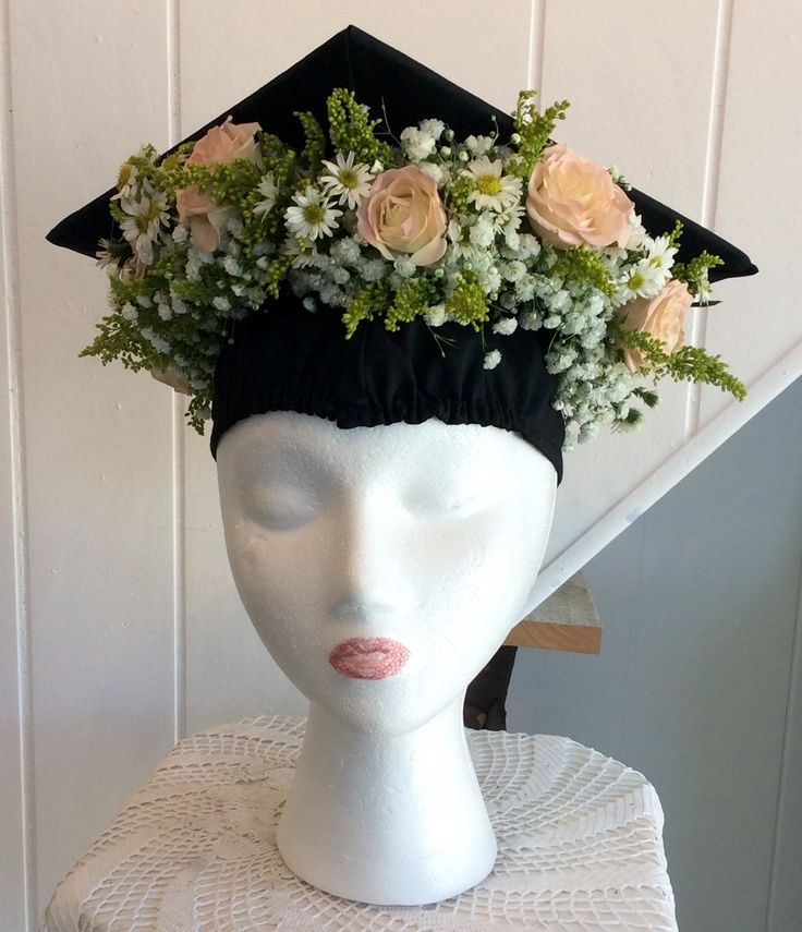 a white mannequin head wearing a black graduation cap with flowers on it's top