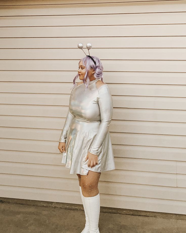 a woman in silver dress and white boots standing next to a garage door with her hands on her hips