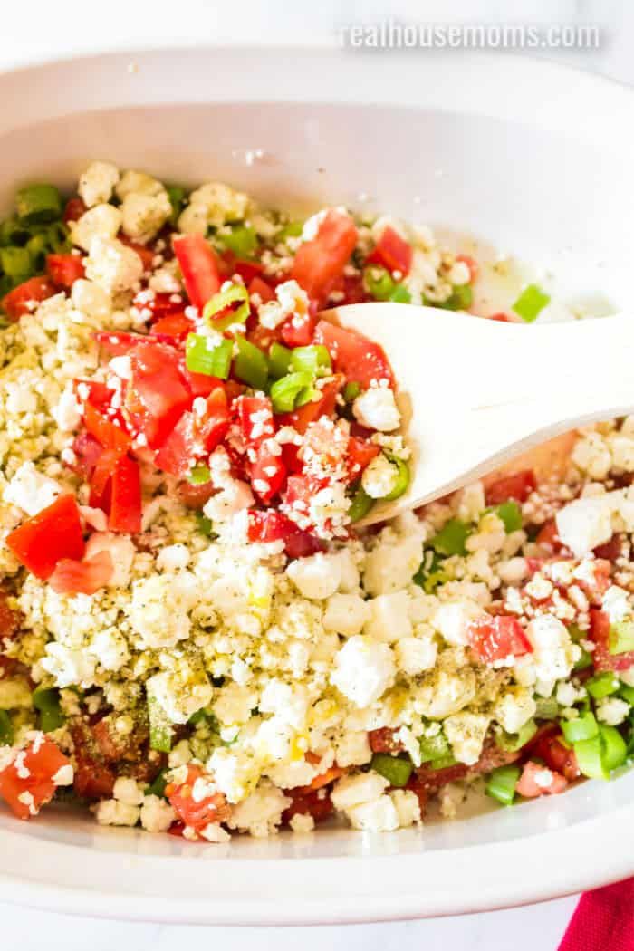 a white bowl filled with chopped vegetables and feta cheese being spooned into it