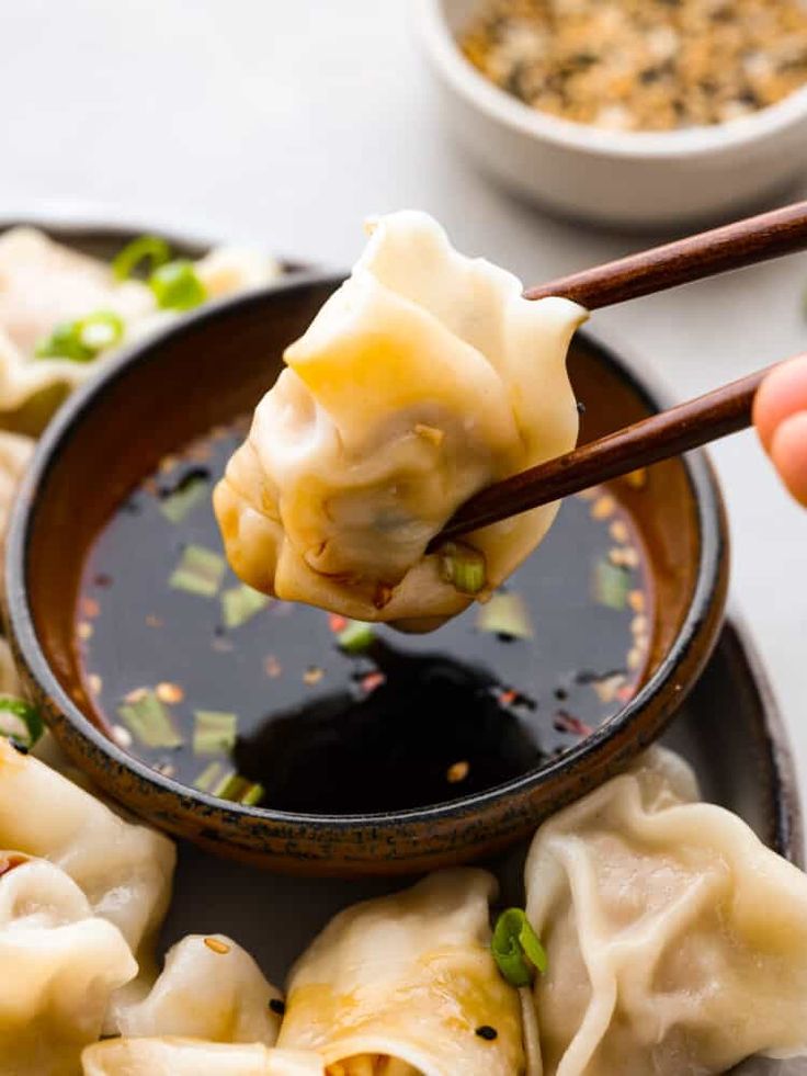 a person holding chopsticks over some dumplings on a plate with dipping sauce