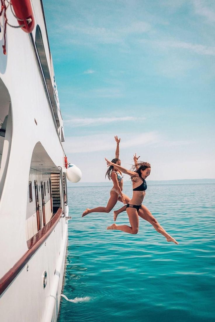 two women jumping off the side of a boat into the ocean