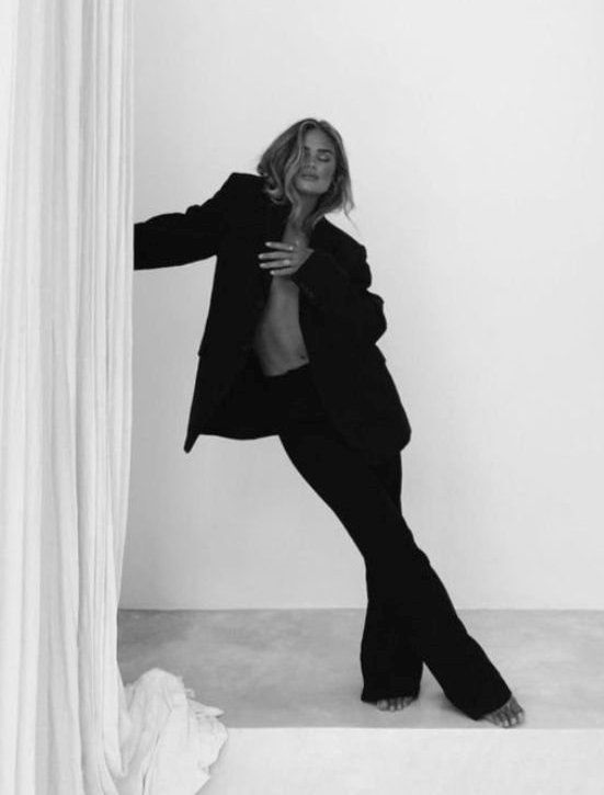 a black and white photo of a woman leaning against a curtain with her hands on her hips