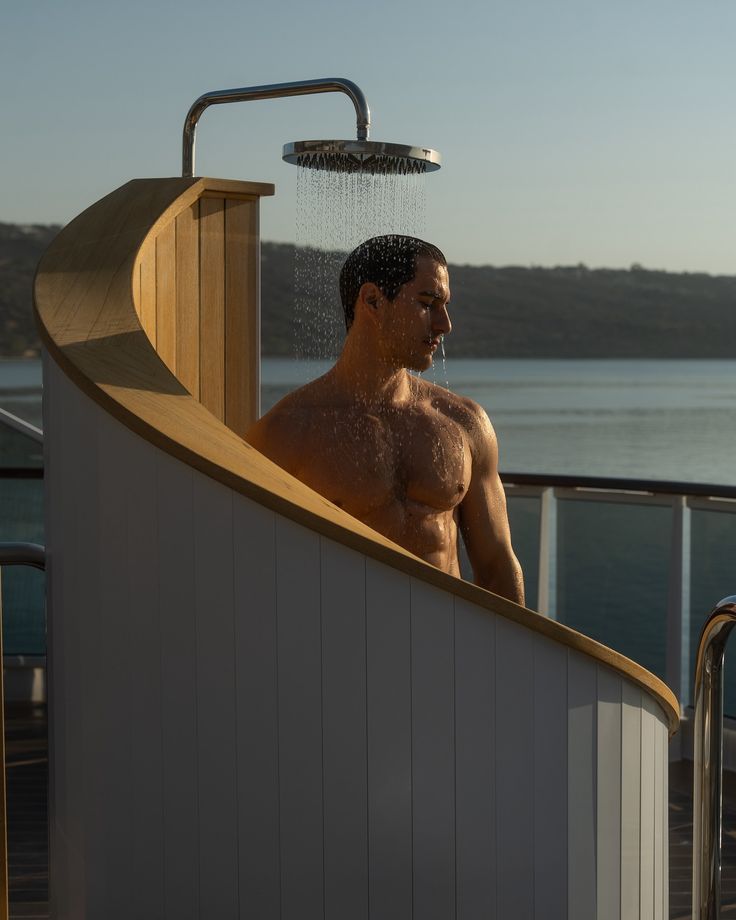 a shirtless man standing in the shower on a cruise ship looking out over the water