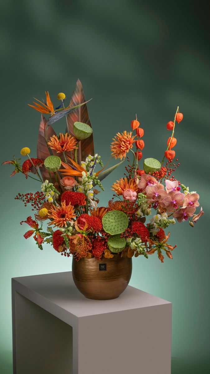 a vase filled with lots of colorful flowers on top of a white pedestal in front of a green background