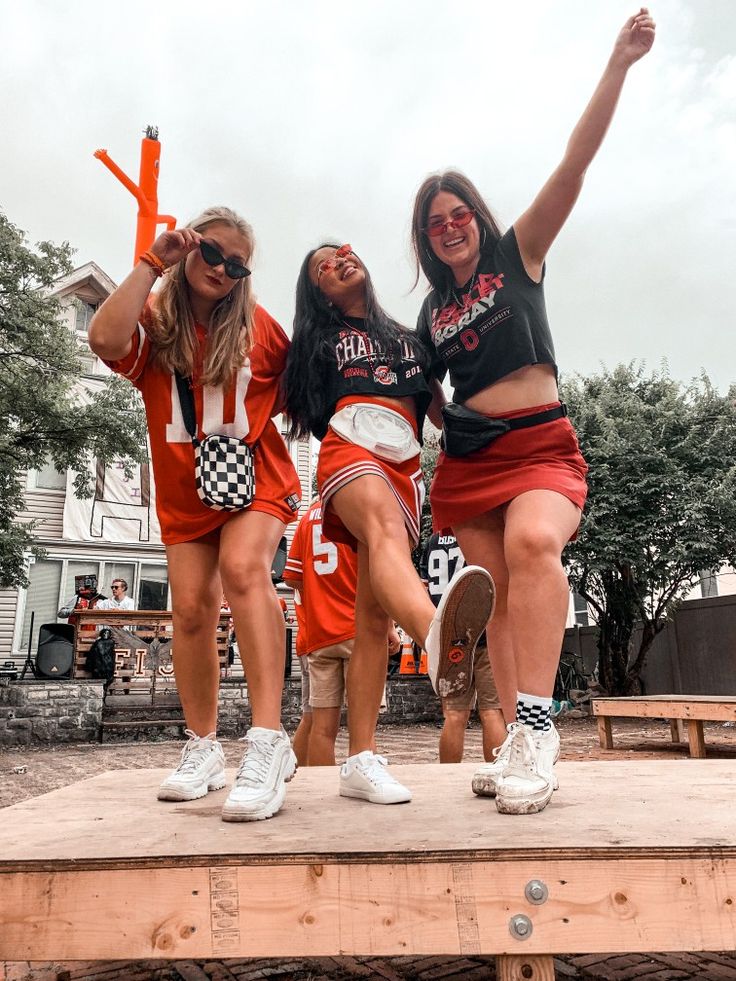 three girls in orange skirts and black shirts are standing on a platform with their arms up