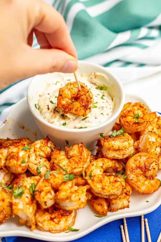 a person dipping sauce onto shrimp on a white plate with skewered toothpicks