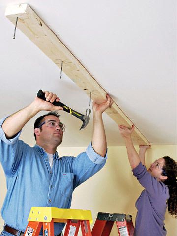 two people are working on the ceiling in their home, one is holding a hammer and the other is using a ladder