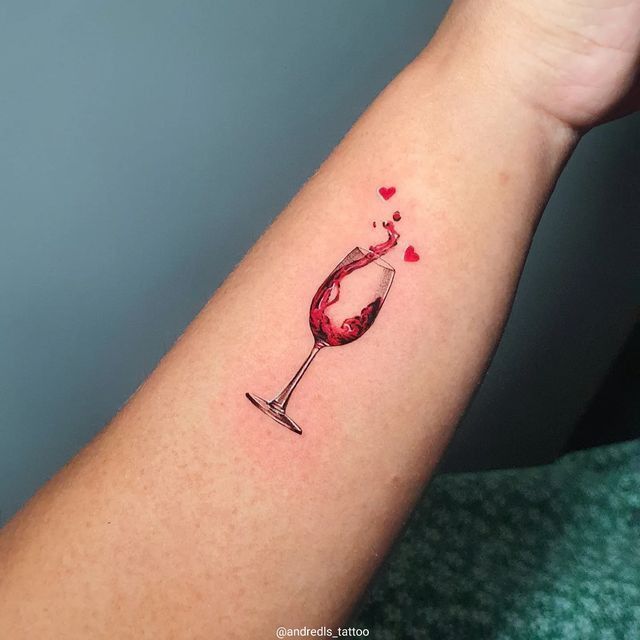 a woman's arm with a glass of wine and hearts tattoo on the wrist