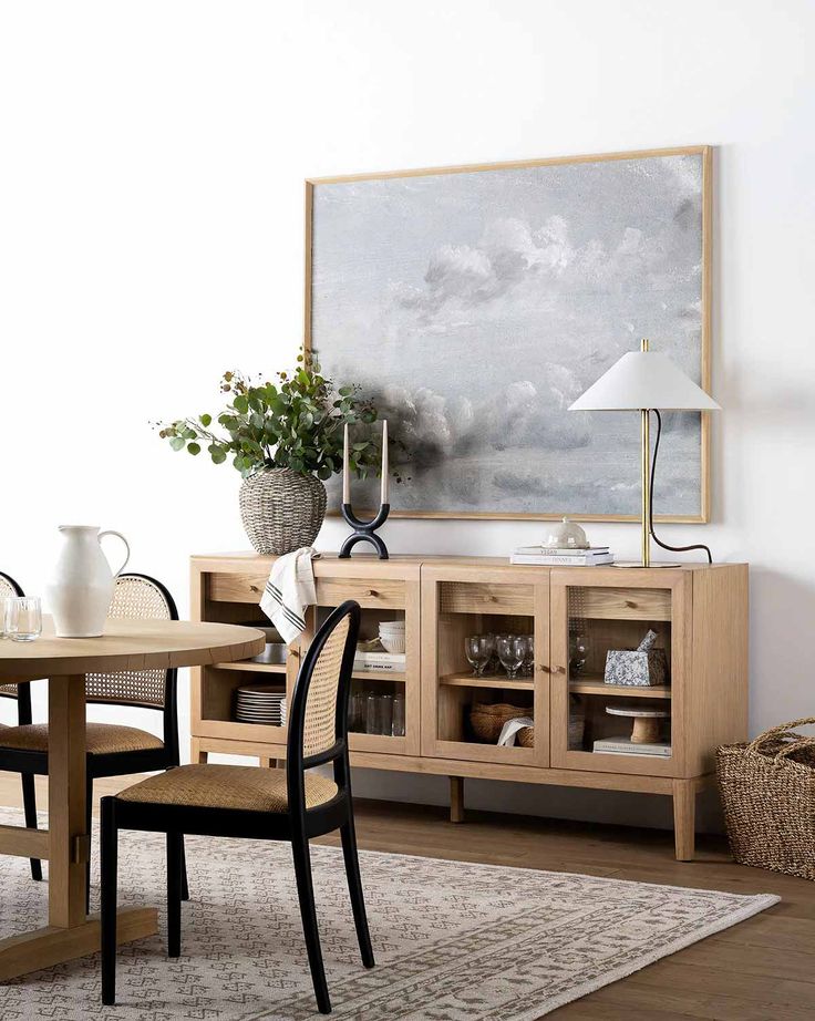 a dining room table and chairs with a painting on the wall behind it, in front of a rug