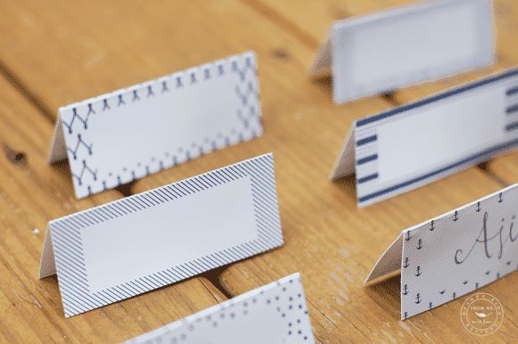 several folded paper place cards on a wooden table with holes in the middle to put name tags