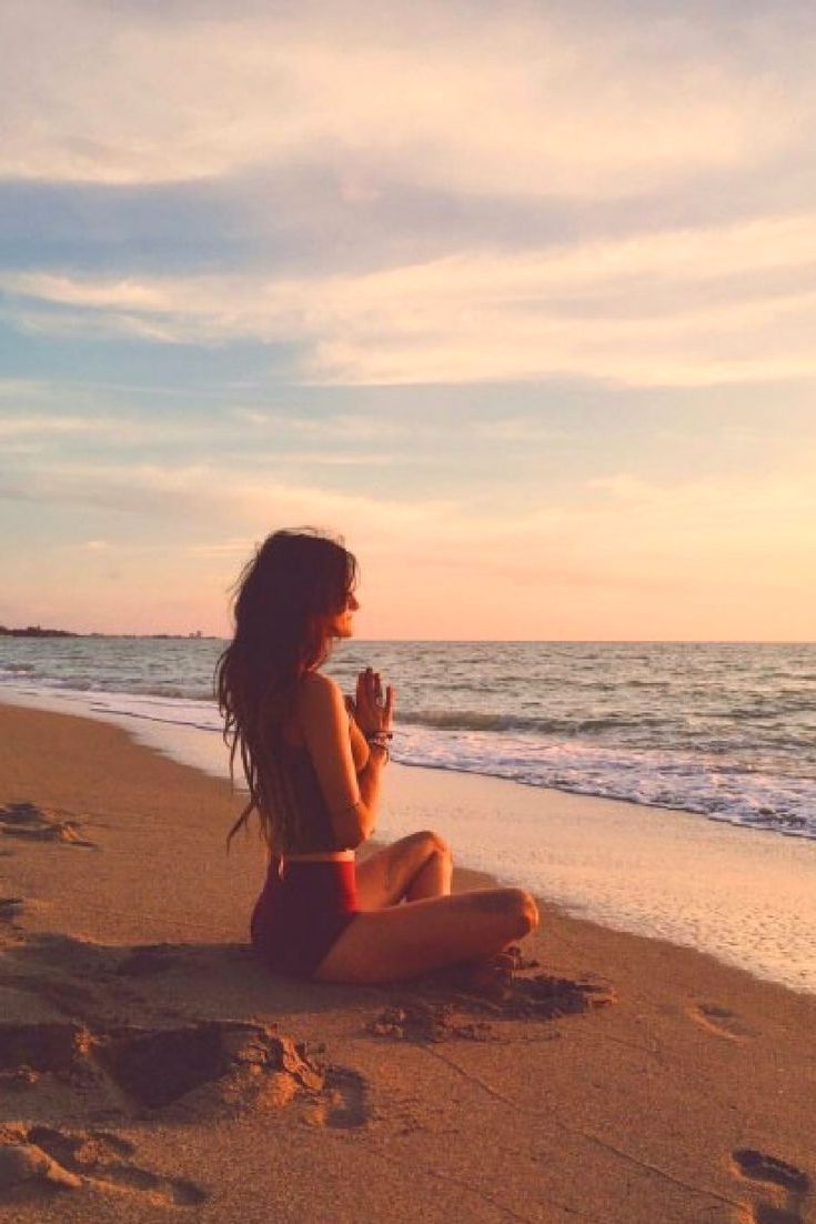 a woman sitting on top of a sandy beach next to the ocean