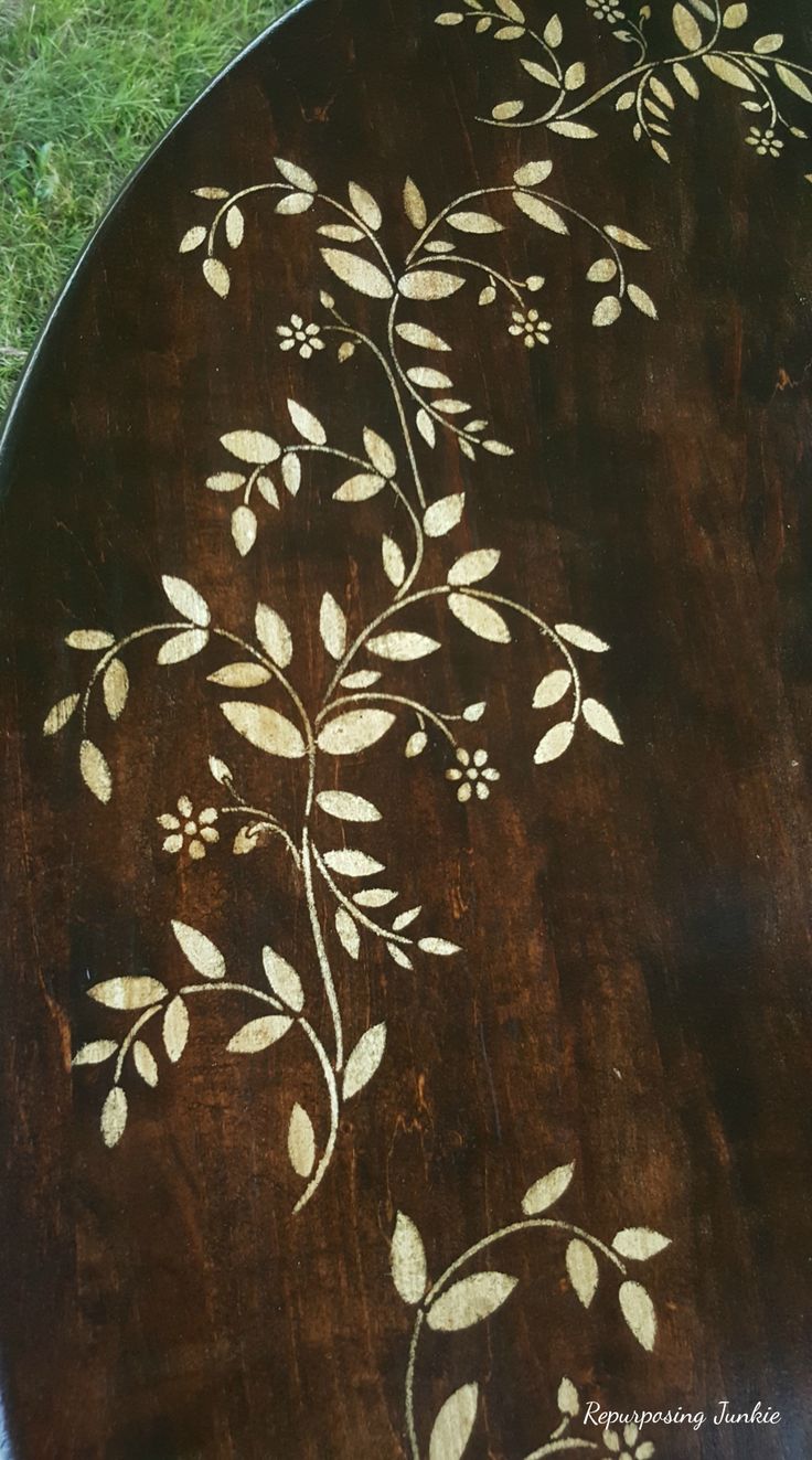 a wooden table with white flowers painted on it and green grass in the back ground