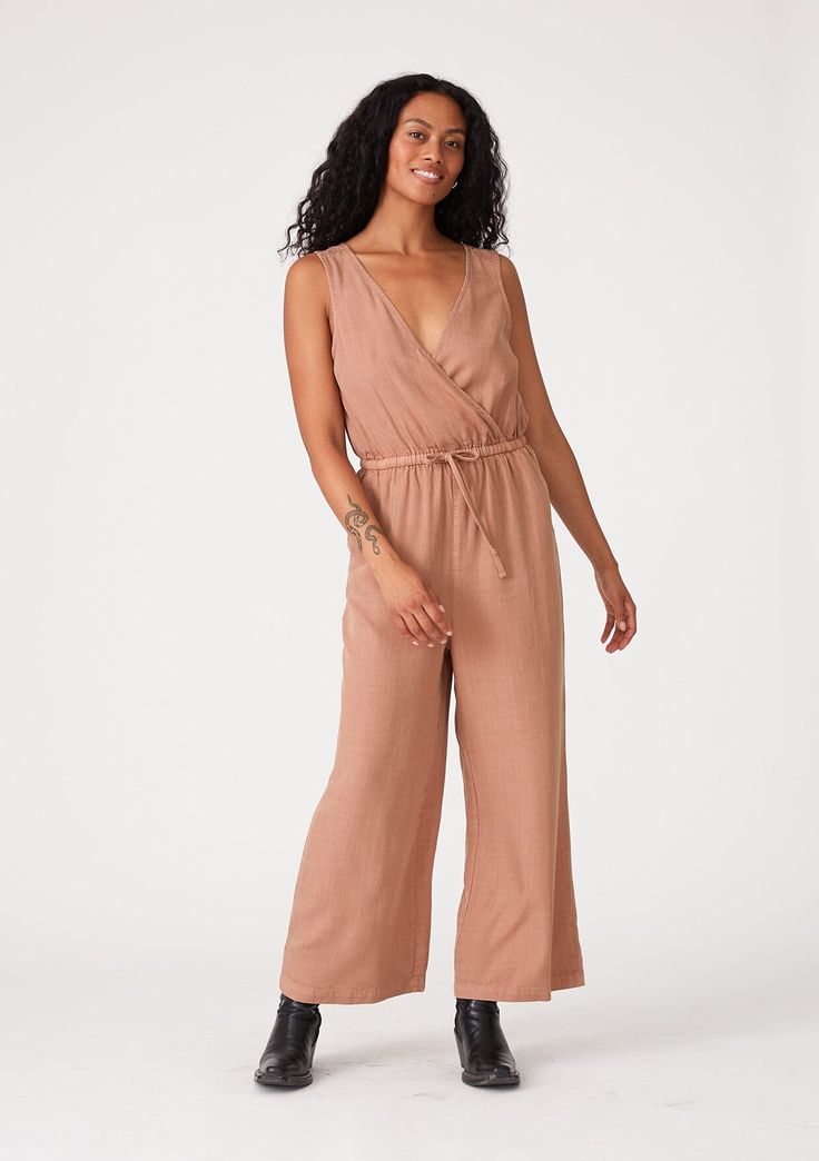 [Color: Clay] A front facing image of a brunette model wearing a pink sleeveless jumpsuit with a cropped wide leg Casual Belted V-neck Jumpsuits And Rompers, Belted V-neck Jumpsuits And Rompers For Vacation, V-neck Belted Jumpsuits And Rompers For Vacation, Belted V-neck Jumpsuit For Vacation, Sleeveless Jumpsuits And Rompers With Tie Fastening For Spring, Casual V-neck Belted Jumpsuits And Rompers, Sleeveless Jumpsuits And Rompers With Tie Waist For Loungewear, Chic Sleeveless Jumpsuits And Rompers With Tie Waist, Summer Sleeveless Jumpsuit With Tie Waist