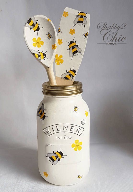 a mason jar with two wooden spoons sticking out of it's lids and bees on the lid