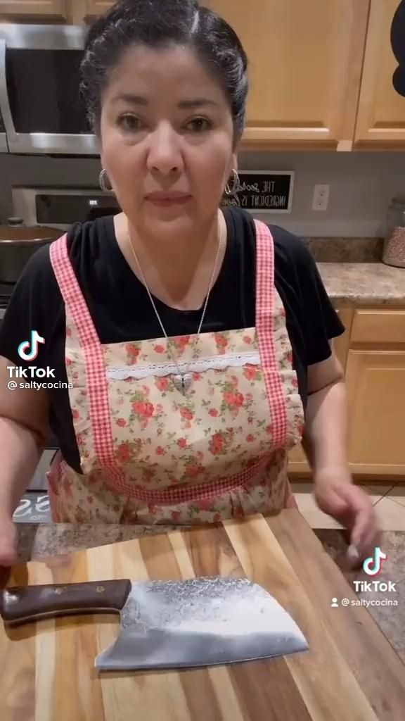 a woman in an apron preparing food on a cutting board with a knife and spatula