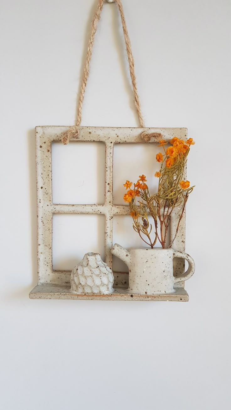 an old window frame with some flowers and a teapot hanging from the side on a rope