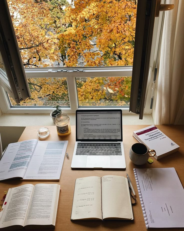 an open laptop computer sitting on top of a wooden desk next to books and papers