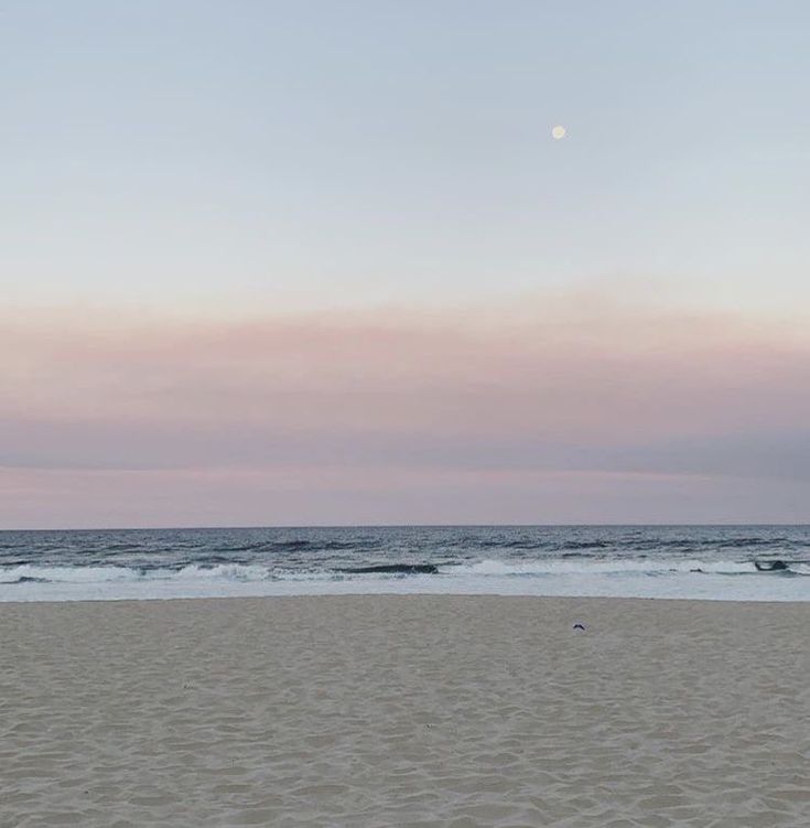 a person walking on the beach with a surfboard in their hand as the sun sets