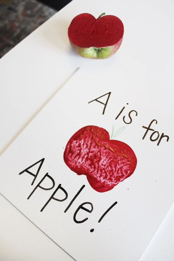 a red apple sitting on top of a white table next to a piece of paper