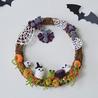 a halloween wreath made with yarn and crochet bats, pumpkins and other decorations