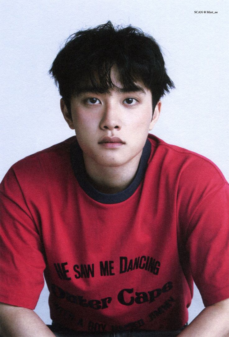 a young man sitting in front of a white wall wearing a red shirt with the words we saw me dancing on it