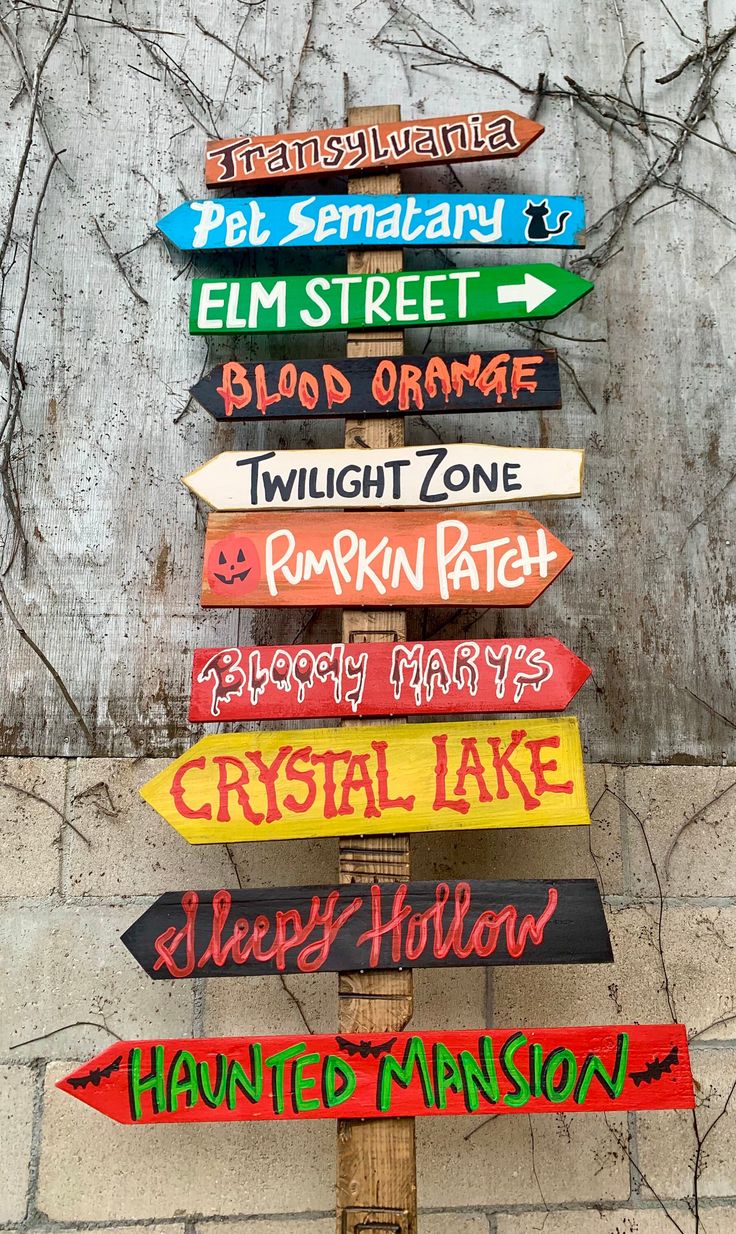 a wooden sign with many different colored signs attached to it's sides on a pole