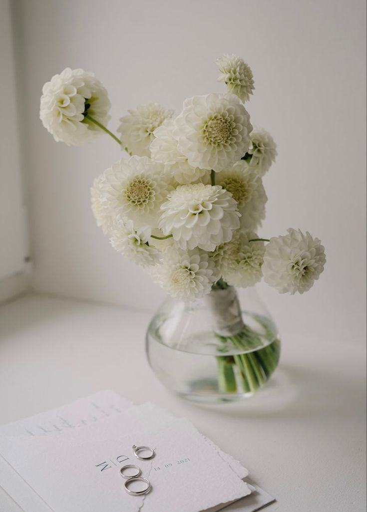 a vase filled with white flowers on top of a table next to a card and envelope