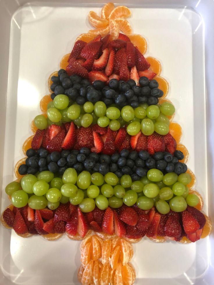 a christmas tree made out of fruit on a white tray with oranges, grapes and strawberries