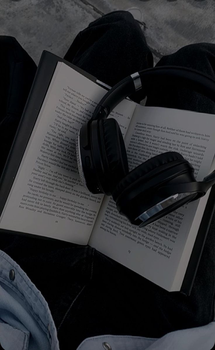 an open book with headphones laying on top of it next to a pair of jeans