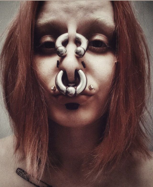 a woman with red hair and piercings on her face is wearing an unusual nose ring