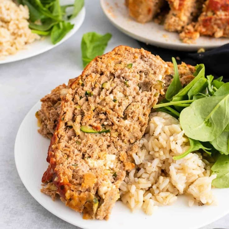 meatloaf with rice and spinach on a white plate next to other food