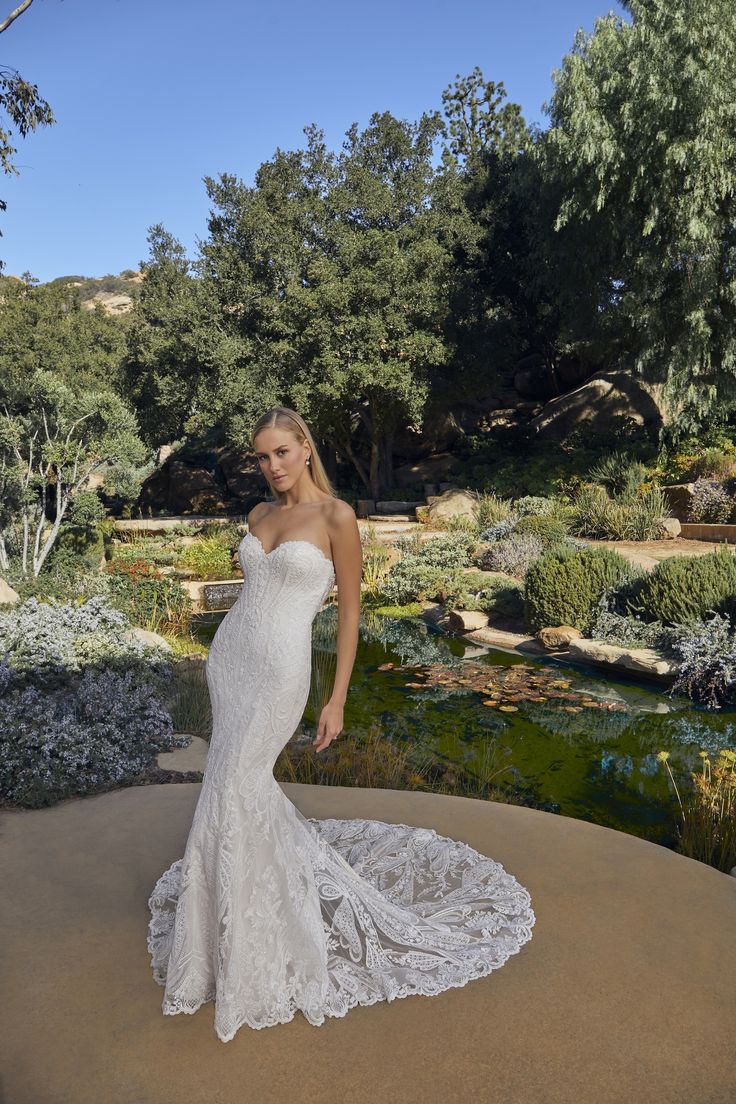 a woman in a white wedding dress standing on a rock near some bushes and trees