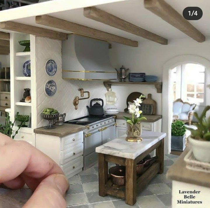 a miniature kitchen with white cabinets and wooden beams on the ceiling is being held up by someone's hand