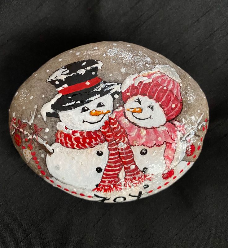 a painted rock with two snowmen and one is wearing a red knitted hat