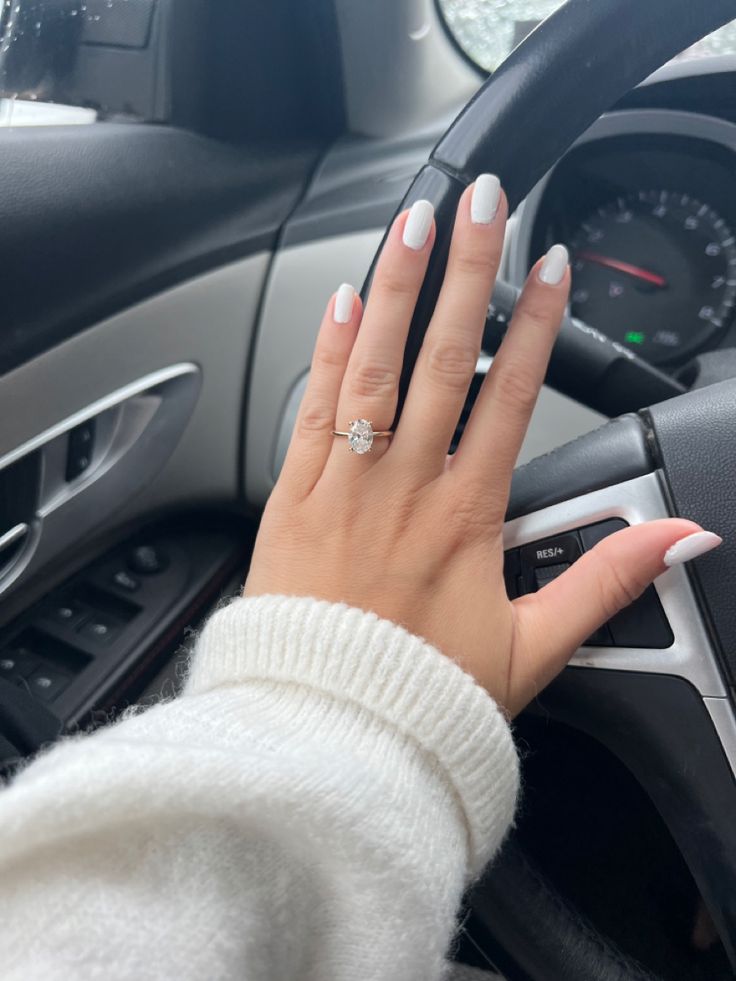 a woman's hand on the steering wheel of a car with her nails painted white