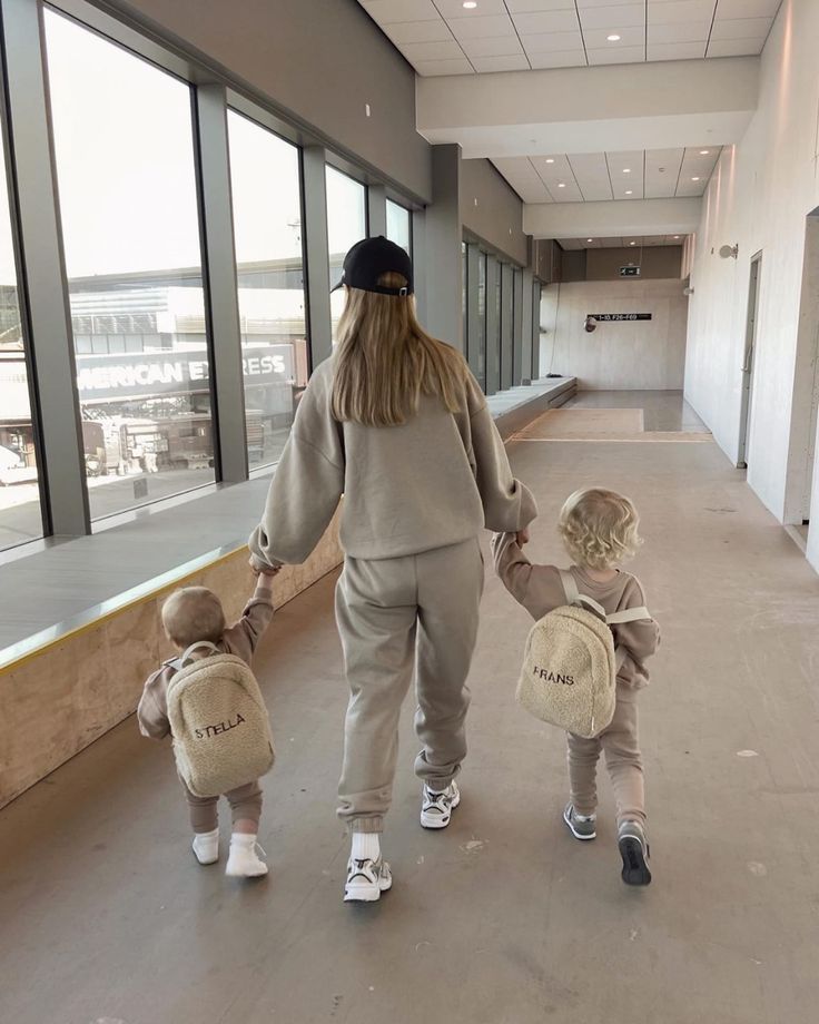 a woman and two children walking down an empty hallway with luggage on their back,