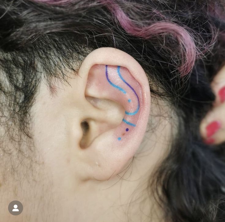 a woman with pink hair has her ear painted in blue and purple lines as if she is listening to music